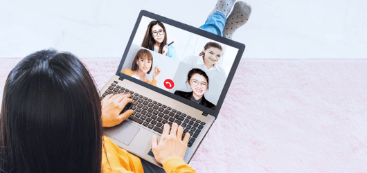 Photo taken from above a sitting woman who has a laptop in her lap. She is talking to a split screen of four other employees about encouraging employee participation.